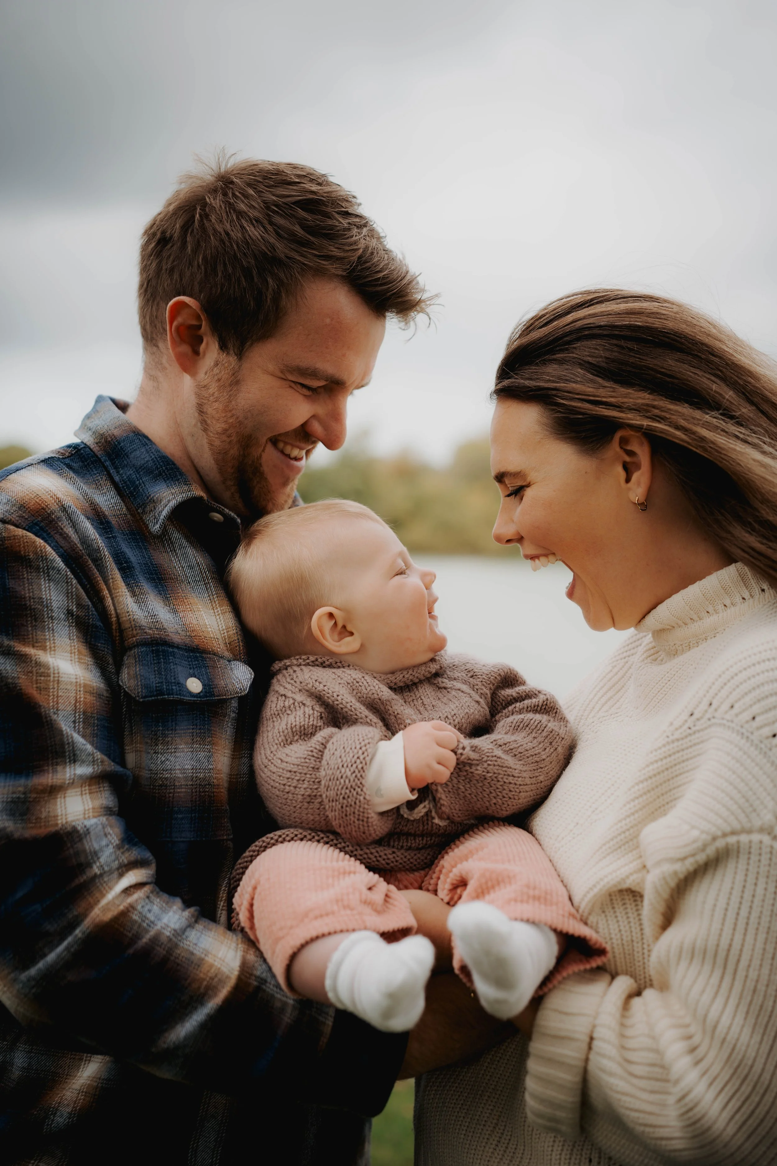 A smiling family of three, a man, woman, and a baby girl, outdoors enjoying a moment together.