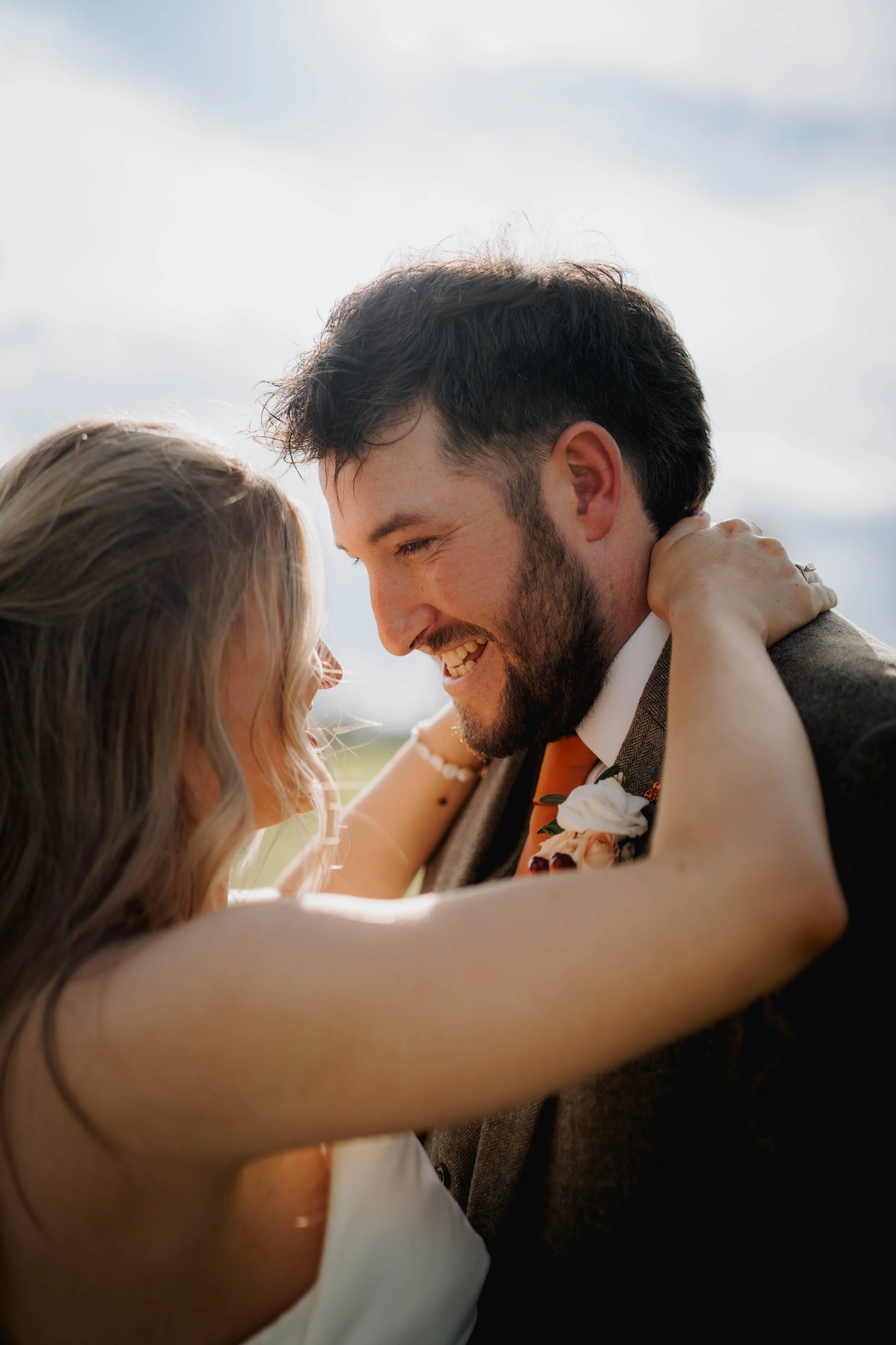 A joyful couple smiling and embracing each other outdoors, with the woman wrapping her arms around the man's neck.