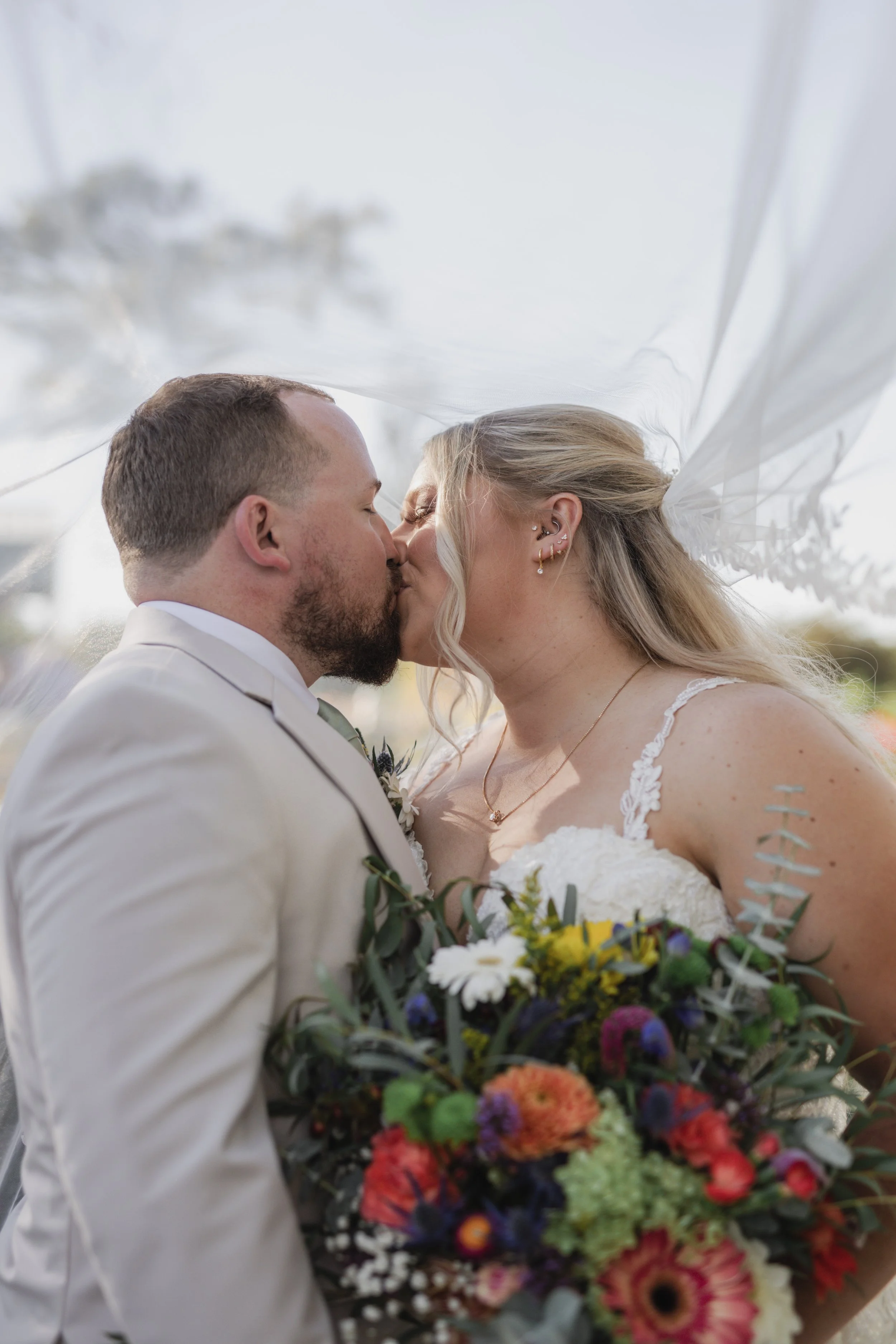 A bride and groom kissing during their wedding, with the bride holding a colorful bouquet of flowers.