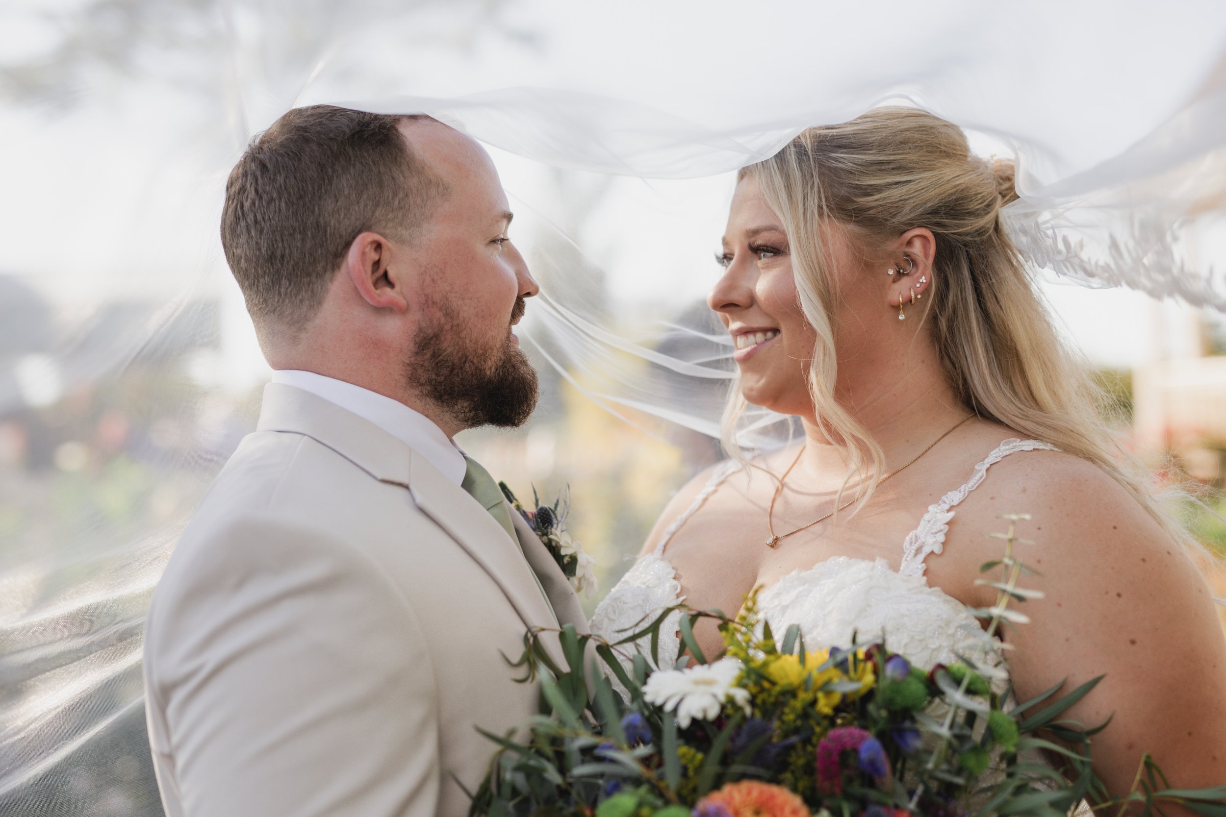 A bride and groom standing close together, looking into each other's eyes during a wedding ceremony, with the bride holding a colorful bouquet of flowers.