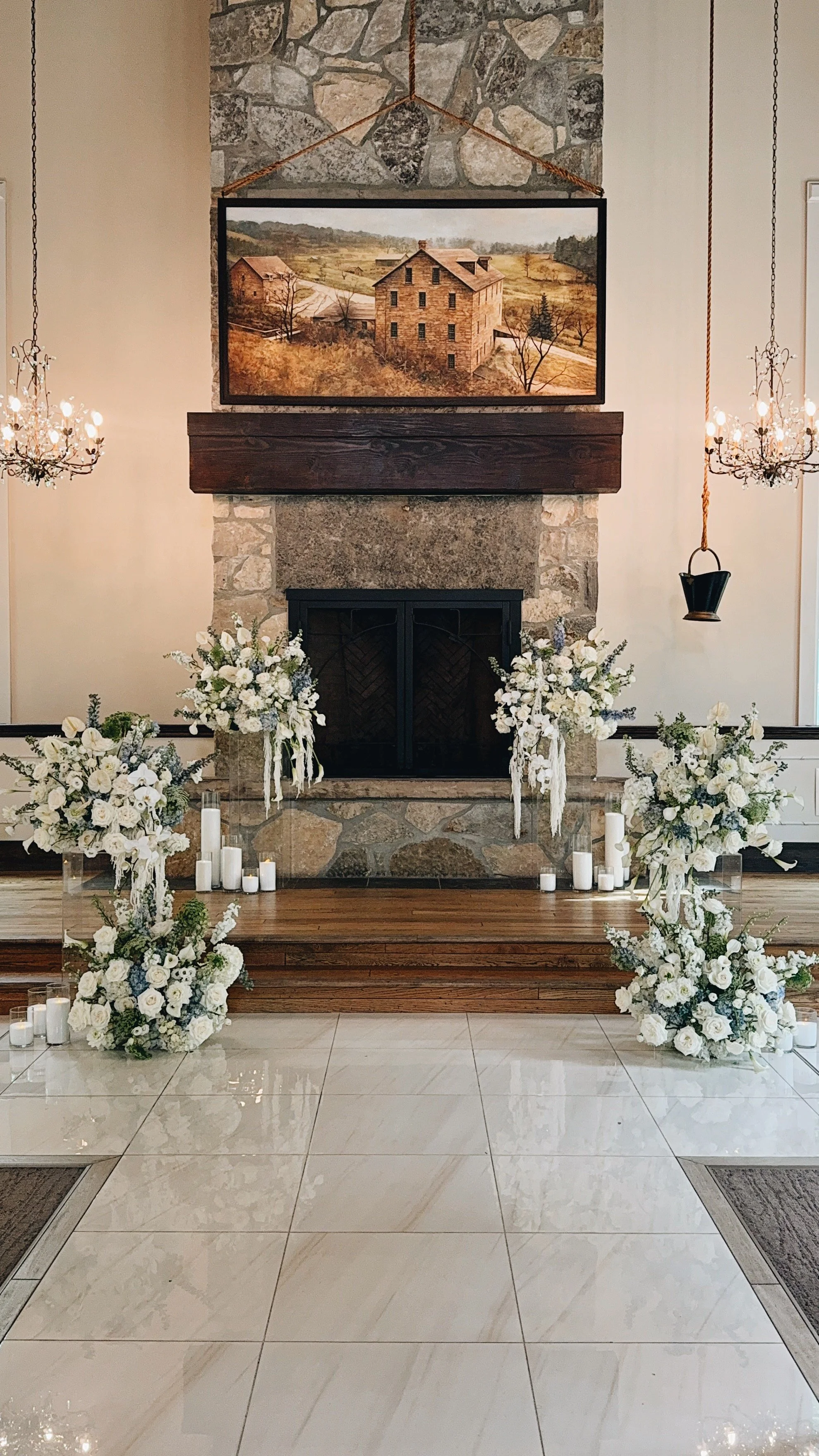 Elegant interior fireplace with floral arrangements, candles, and chandeliers, decorated for a wedding or special event.