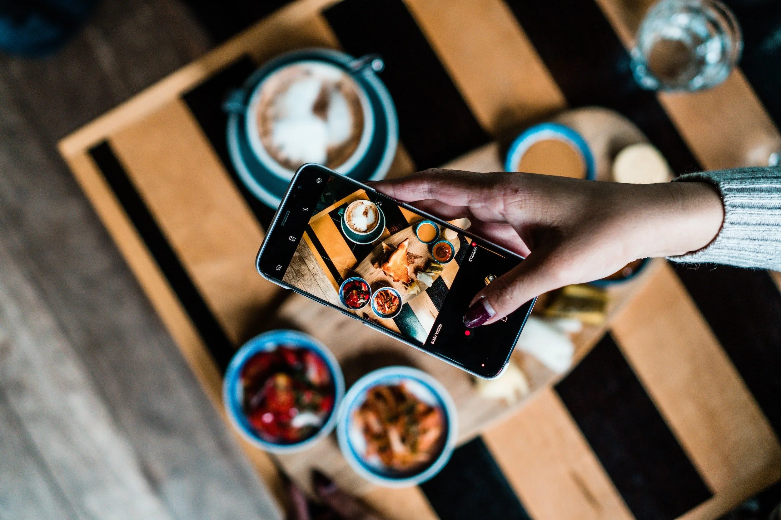 Person taking a photo of a food display on a wooden table with a smartphone.