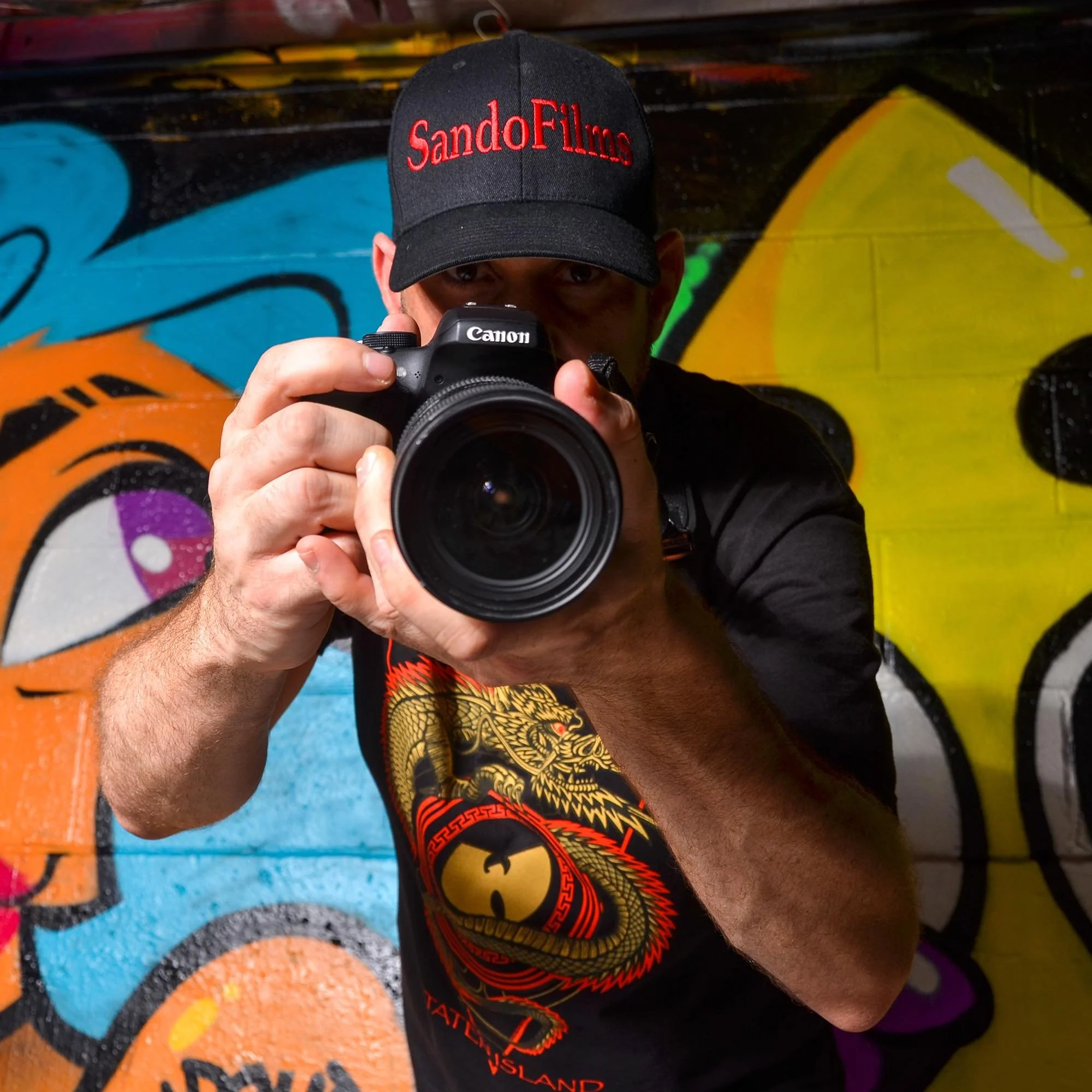 A man taking a photograph with a Canon camera in front of a colorful graffiti wall.