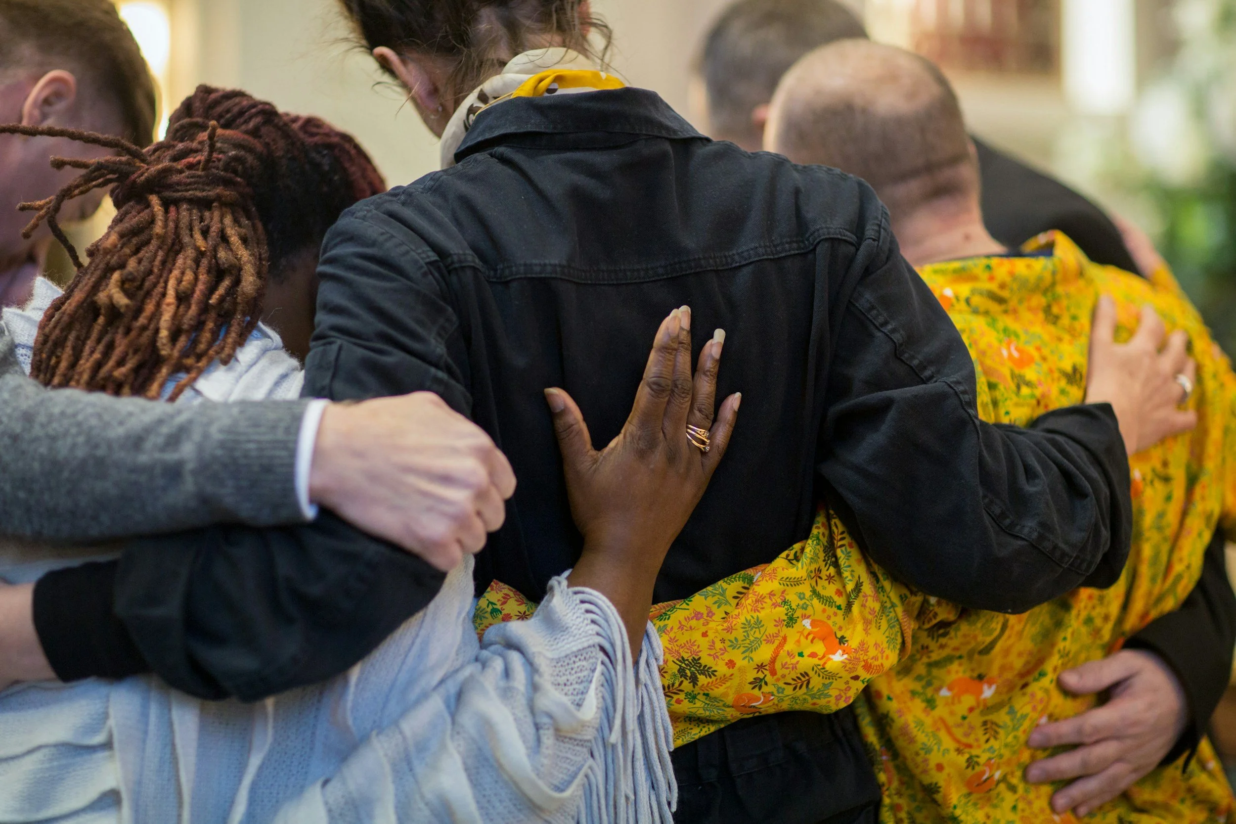 Grief Coaching Wellington. People praying with their hands on each other's shoulders and backs, showing unity and compassion.