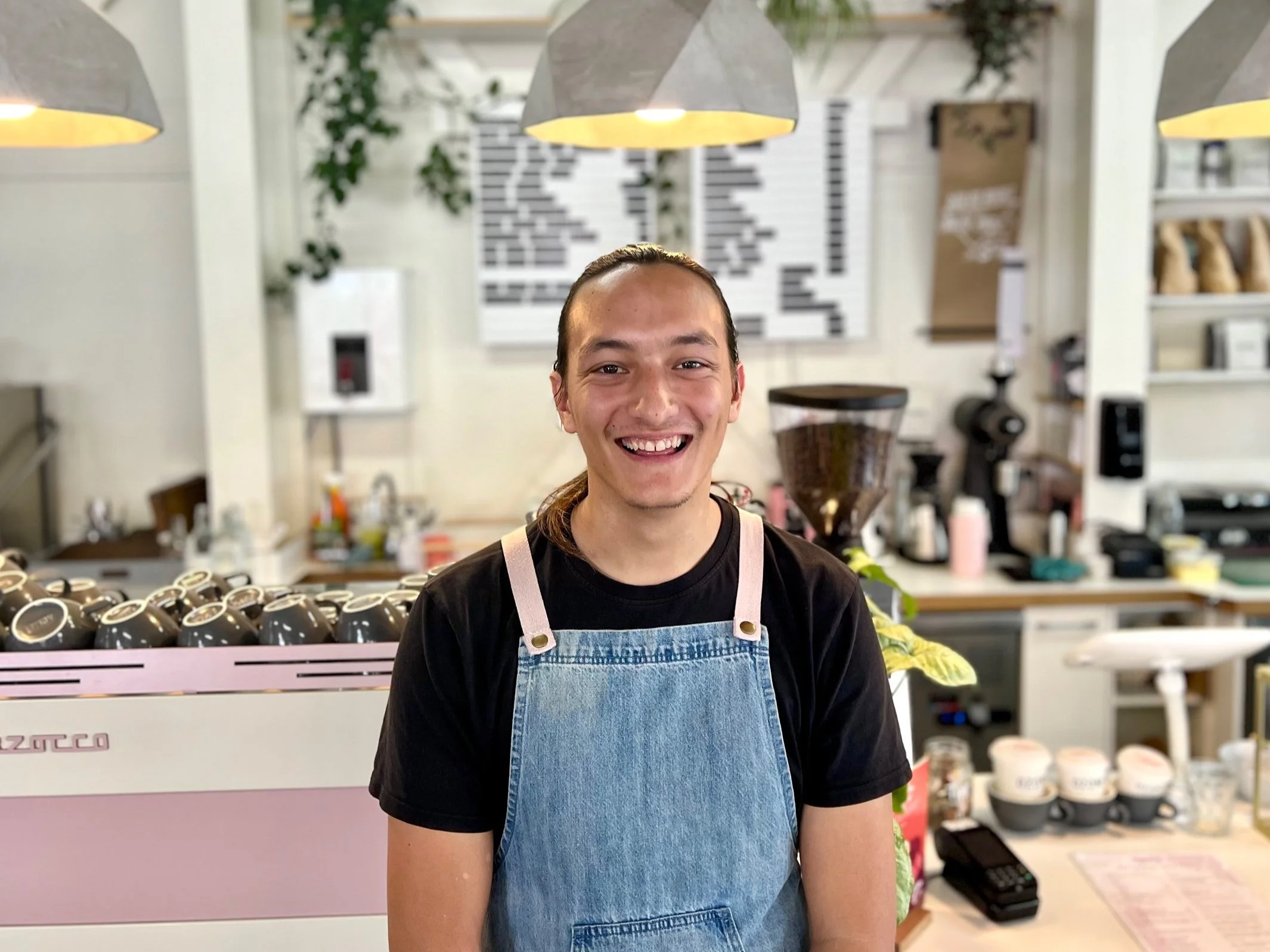A smiling barista in front of a coffee machine