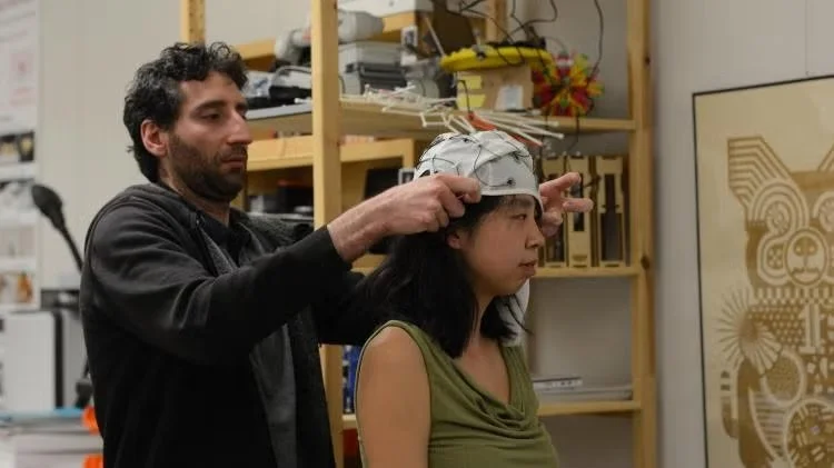 El investigador Tiago Roque coloca un casco de electroencefalografía (EEG) a una participante, su colega Ellen Yi-Luen Do,  para registrar sus ondas cerebrales durante el experimento.