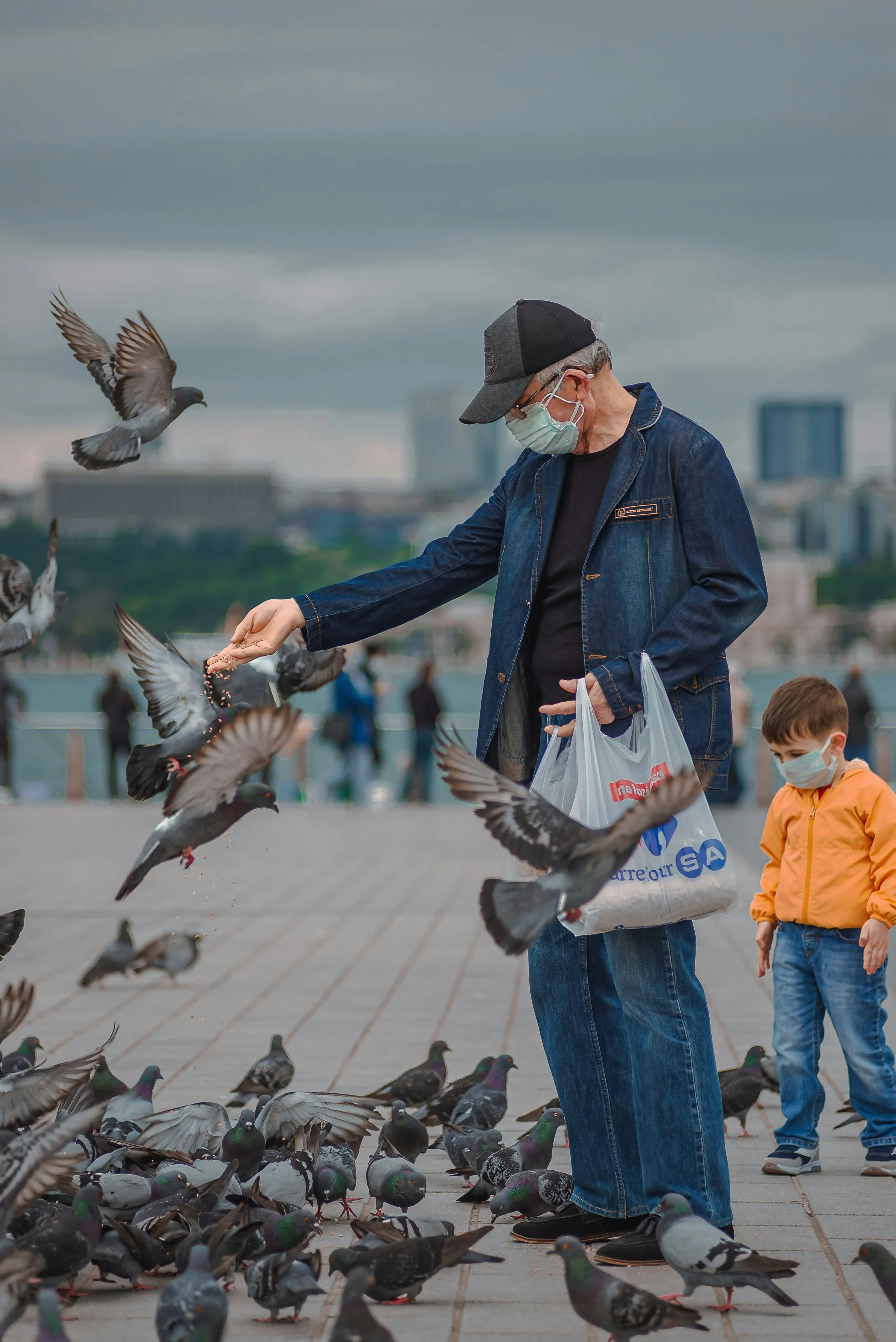 Un hombre alimenta palomas junto a un niño en un espacio urbano.