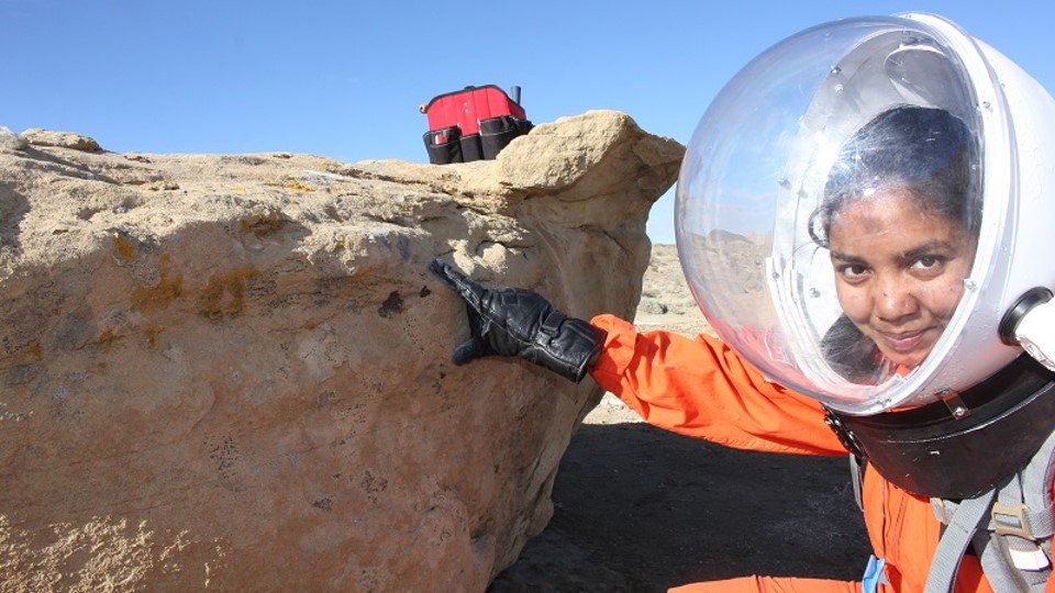 La bióloga de la tripulación Anushree Srivastava recolecta líquenes cerca de la Estación de Investigación del Desierto de Marte, con un traje espacial simulado.