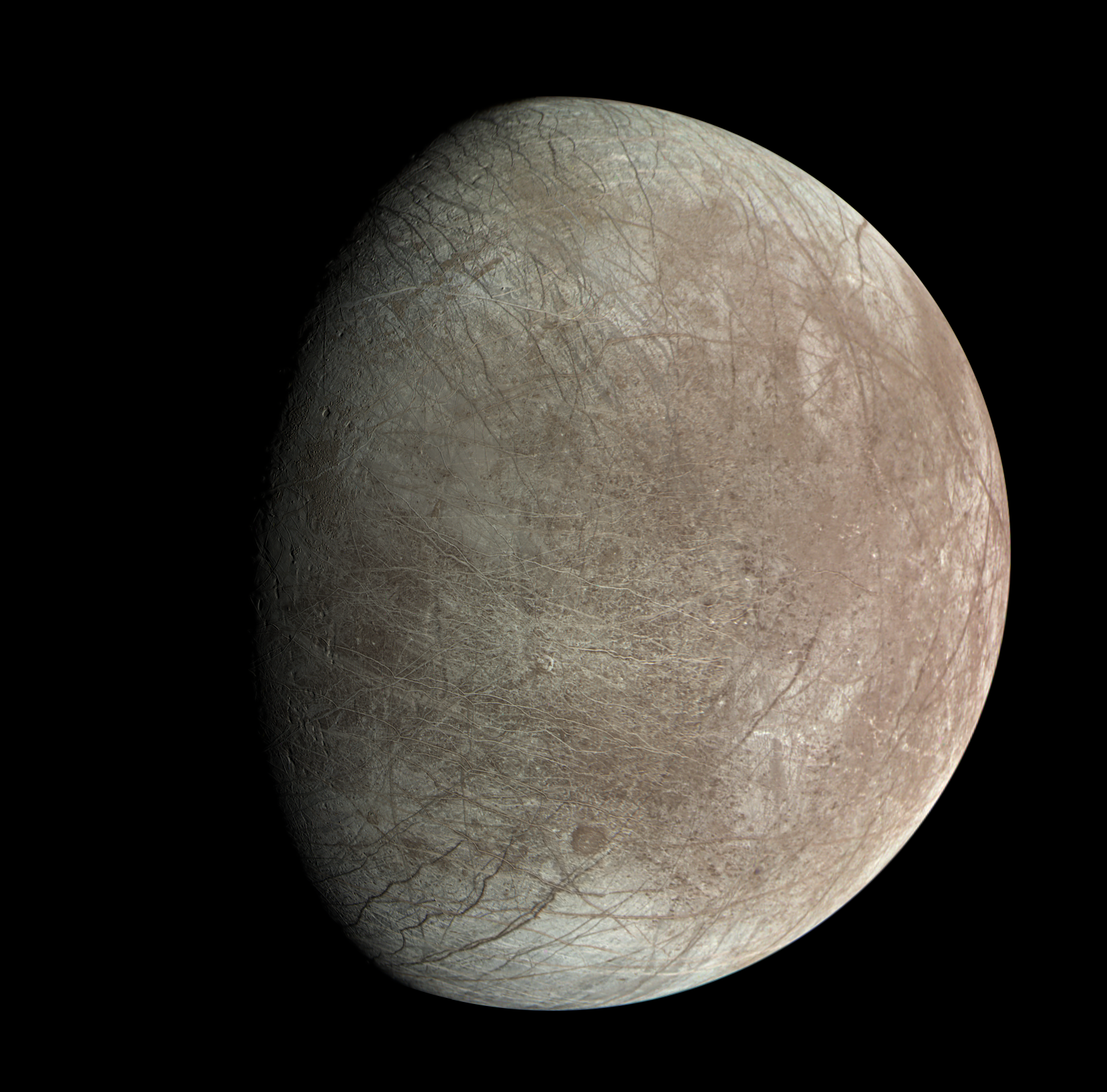 Europa, fotografiada por la sonda Juno de la NASA, muestra una superficie surcada por una compleja red de grietas y fracturas que delatan la presencia de un océano global oculto bajo el hielo.