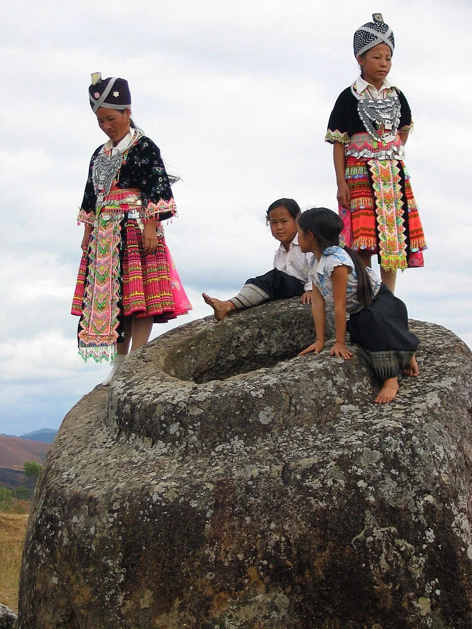 Mujeres y niñas hmong posan sobre una de las gigantescas vasijas de piedra del yacimiento 1 del páramo de las tinajas.