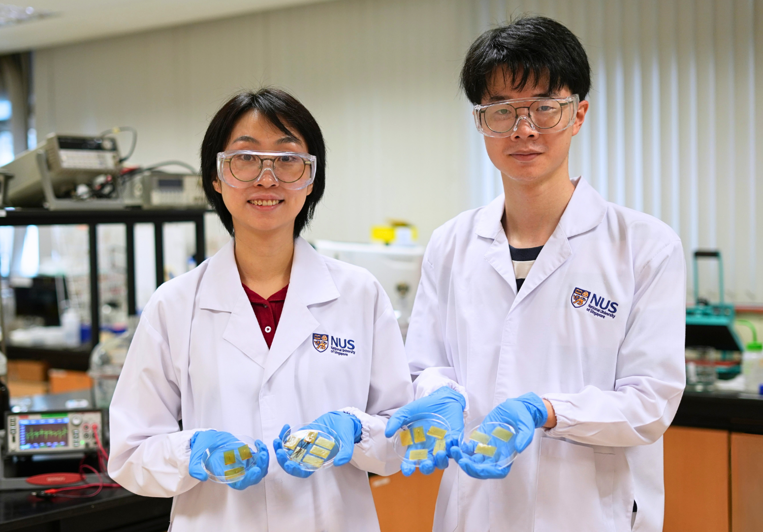 El profesor Yu Jun Tan (izquierda) y el doctorando Zhou Jinrun muestran varios prototipos de la nueva piel electrónica autorreparable, capaz de detectar el contacto, identificar daños y recuperar su funcionamiento incluso bajo el agua.