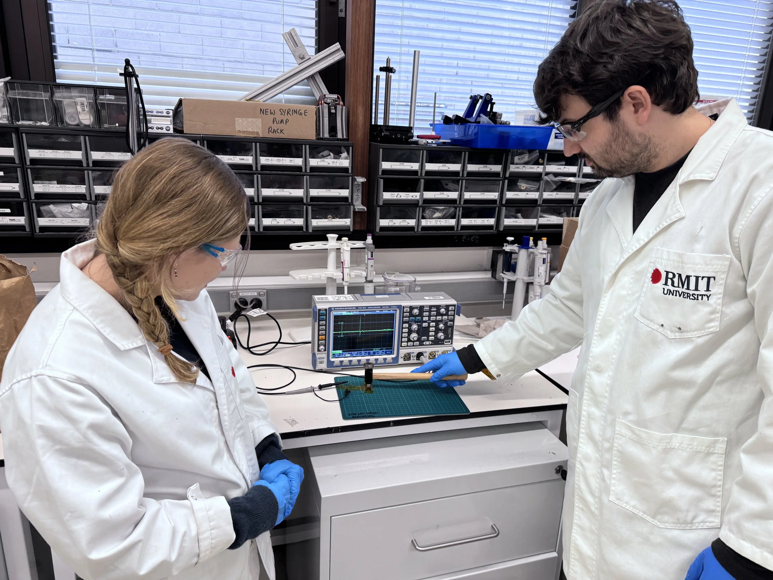 Los investigadores de RMIT Robert Komljenovic y Yemima Ehrnst preparan una prueba de impacto con martillo para comprobar la durabilidad del dispositivo de nailon generador de electricidad.
