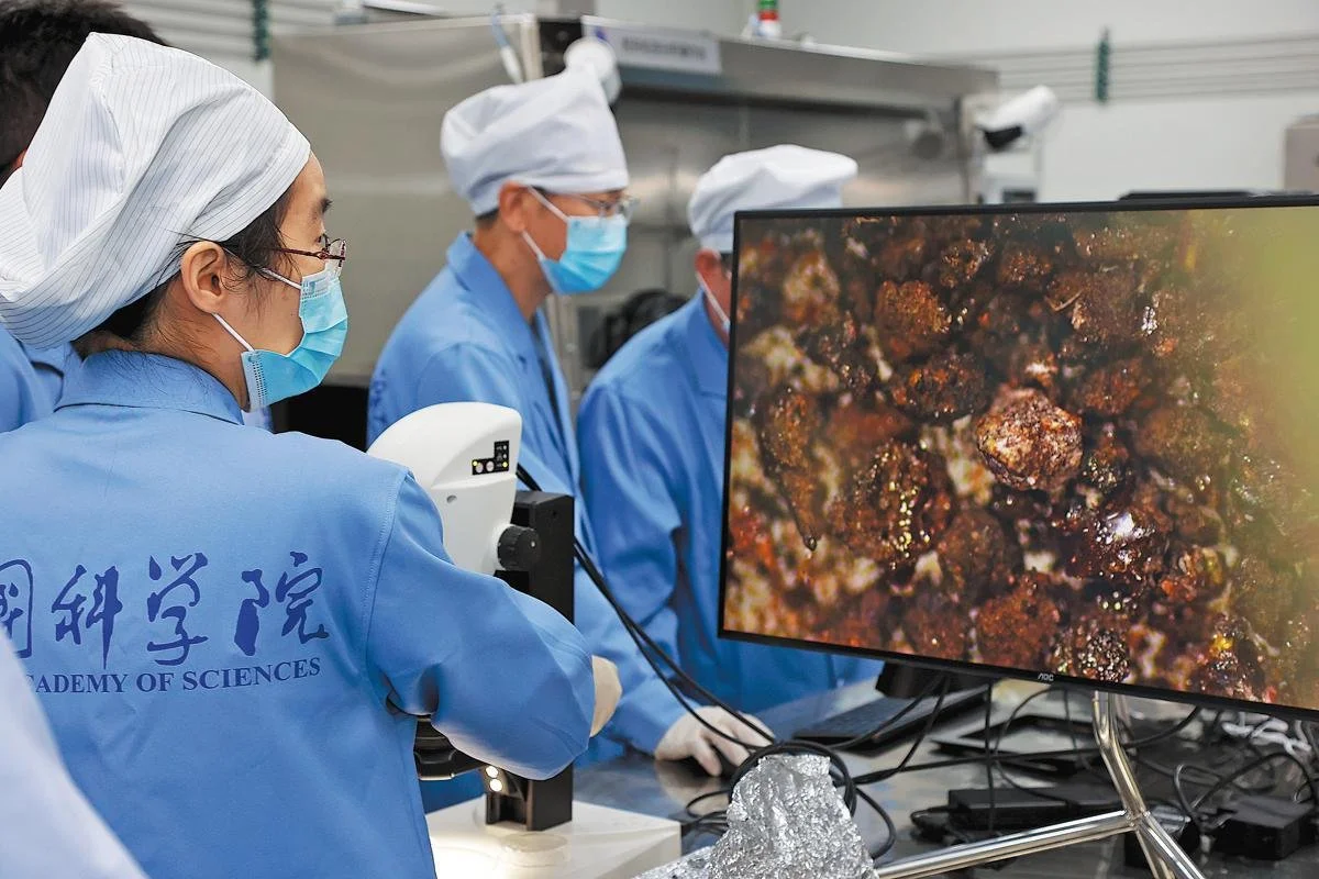 Investigadores de la Academia China de Ciencias analizan al microscopio las diminutas muestras de roca y regolito recogidas por la misión Chang'e-6 en la cara oculta de la Luna.