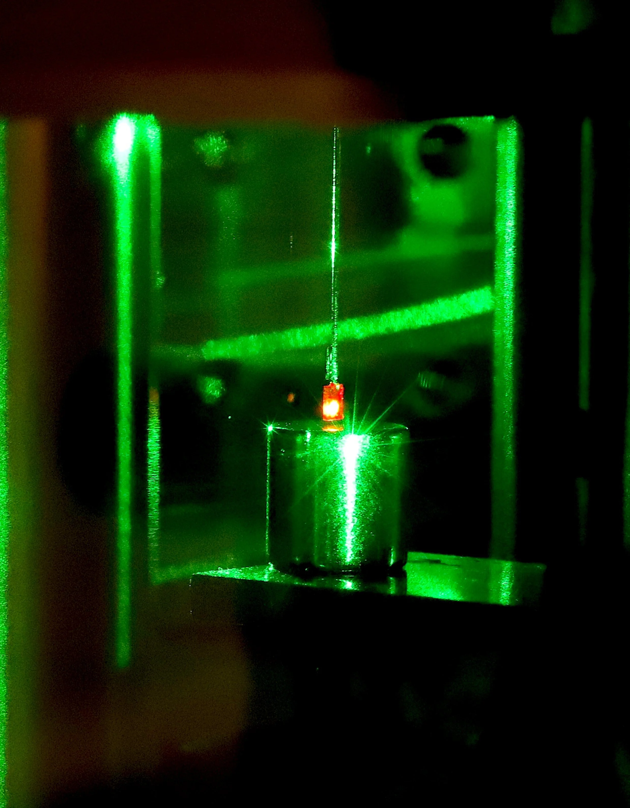 El diamante brilla en rojo al recibir la luz de un láser verde. Los pulsos modifican los estados de espín de sus electrones y generan un diminuto empuje hacia el imán situado debajo.