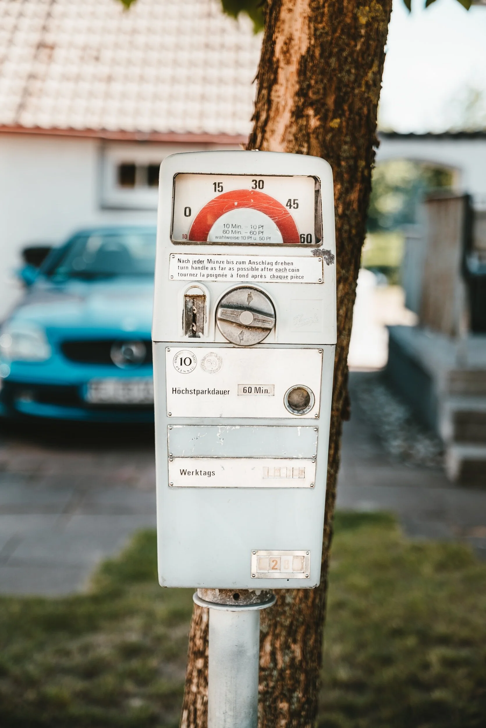 Vintage parking disc payment station mounted on a pole next to a tree, with a blue car parked in the background.