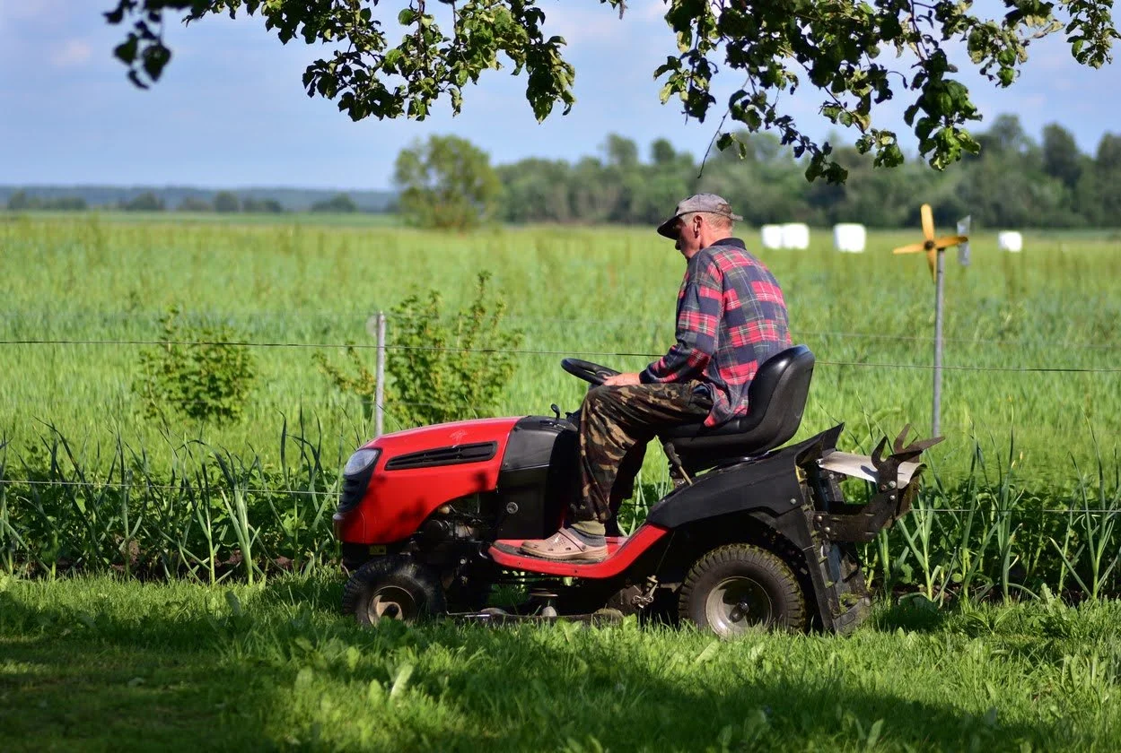 Man on red riding lawnmower mowing country lawn.