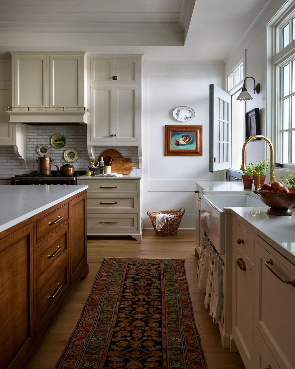 A cozy kitchen with white cabinets, a custom wooden island, a rug, a dutch door and a large window with sunlight.