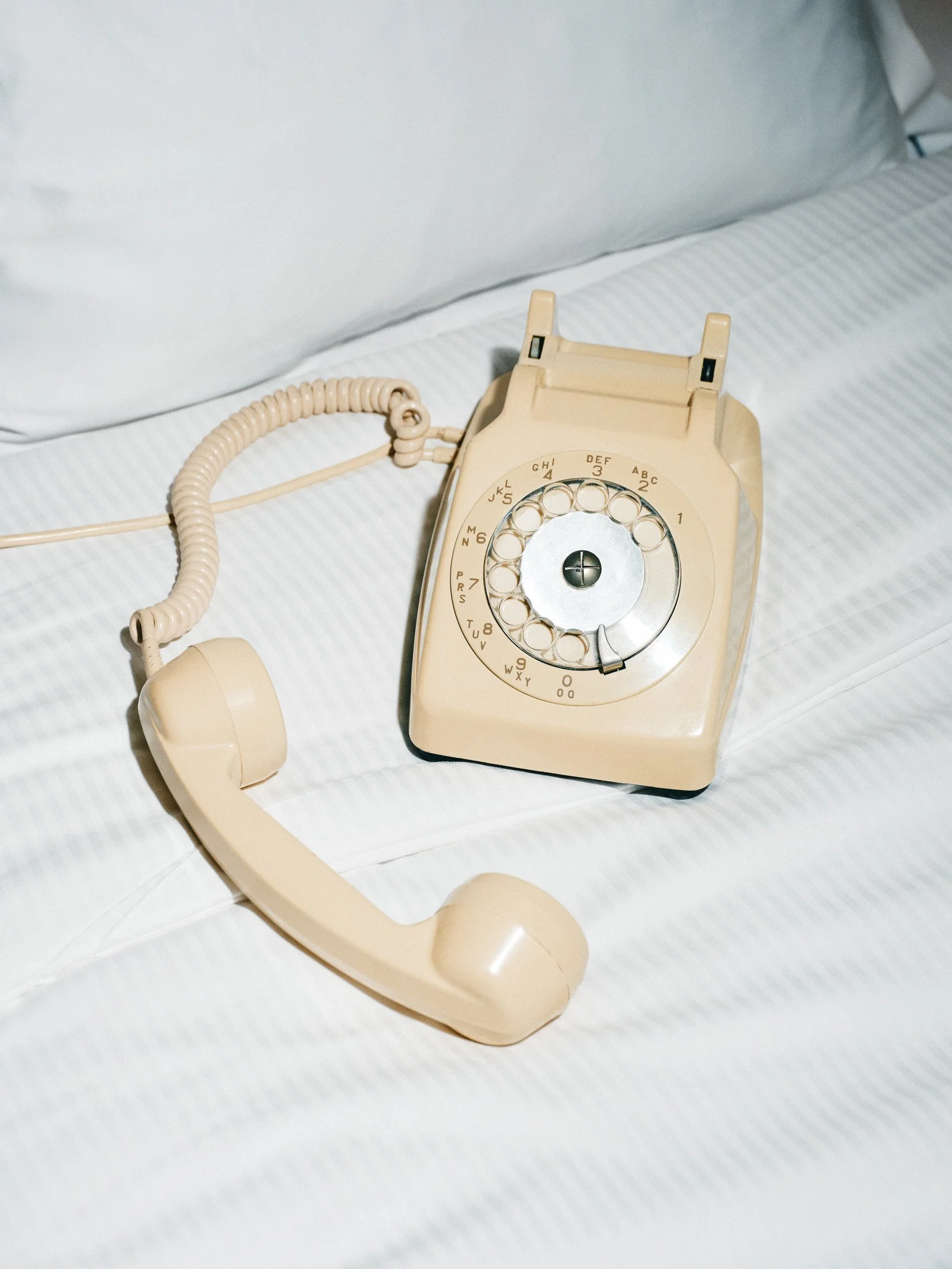 A person's arm extended to hold a green vintage telephone receiver by its cord against a cloudy sky background.