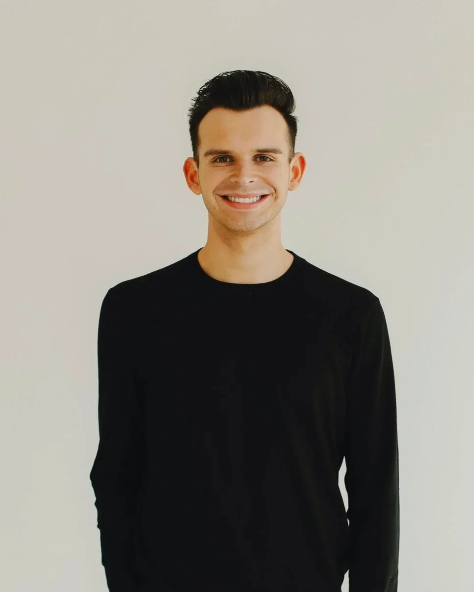 Smiling person in a black shirt against a plain background.