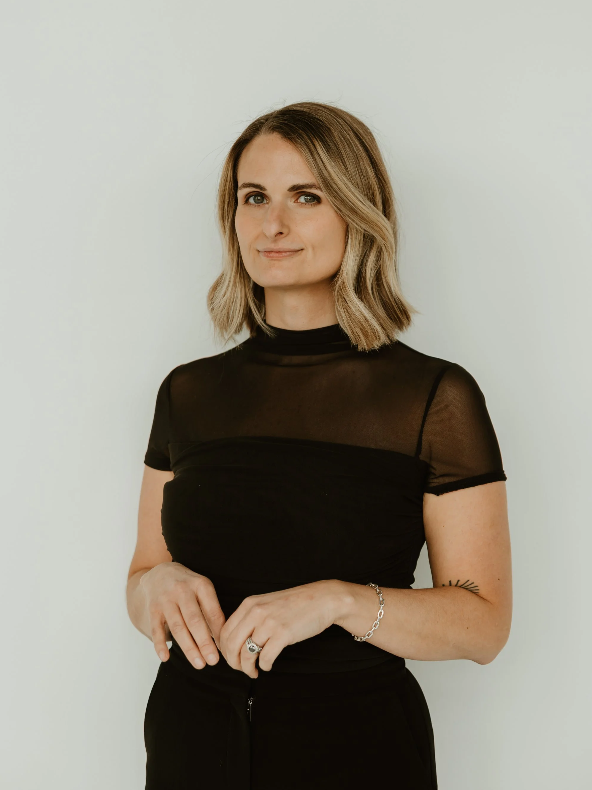 Smiling woman in black top with long hair against a plain background.