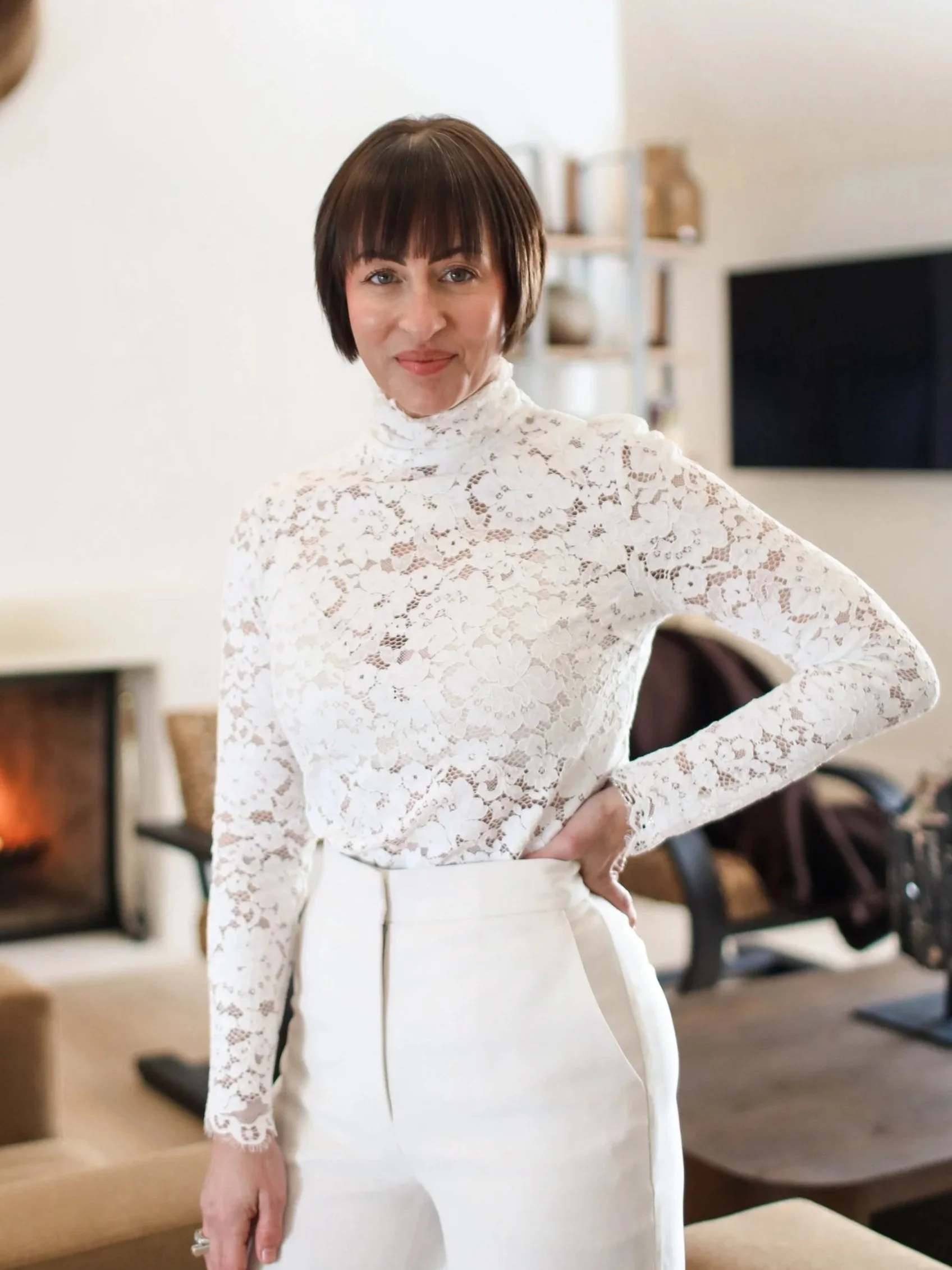 Smiling person with short, light-colored hair wearing a white blouse.