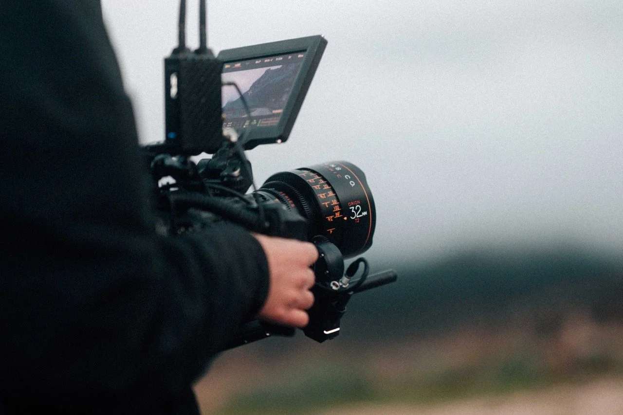 Close-up of a person operating a professional camera with a large lens outdoors during cloudy weather.