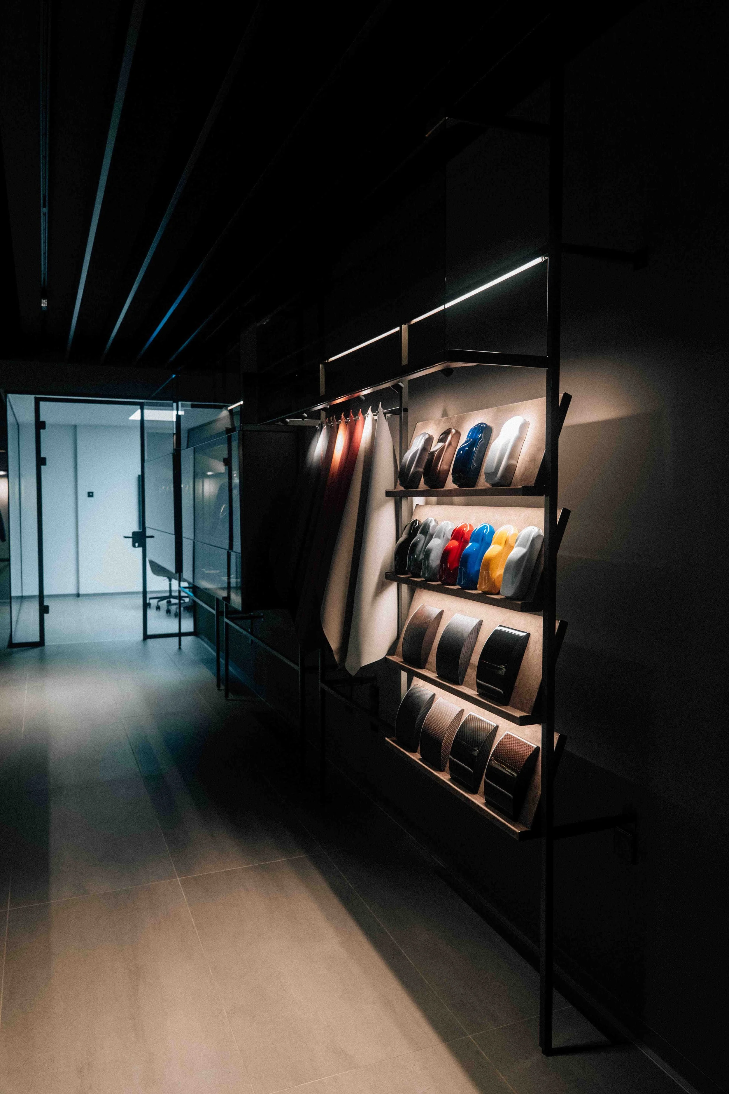 Display of motorcycle or scooter helmets on a wall in a modern, sleek showroom with dim lighting.