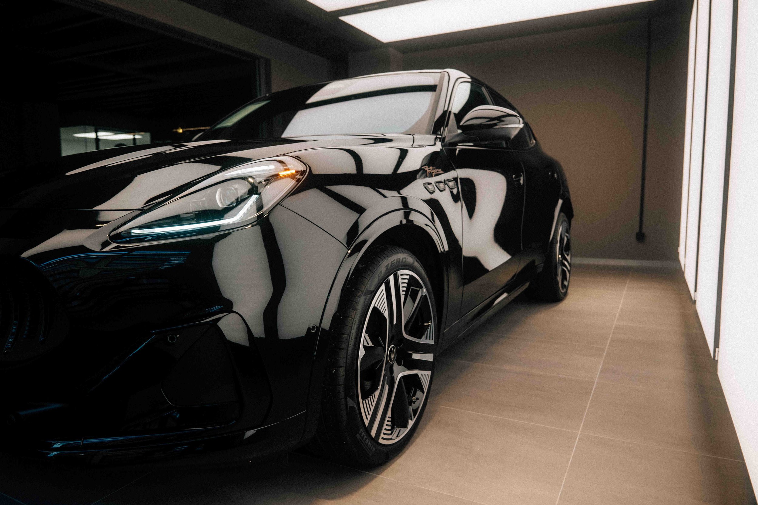 Black luxury car inside a modern garage with wooden flooring and white walls.