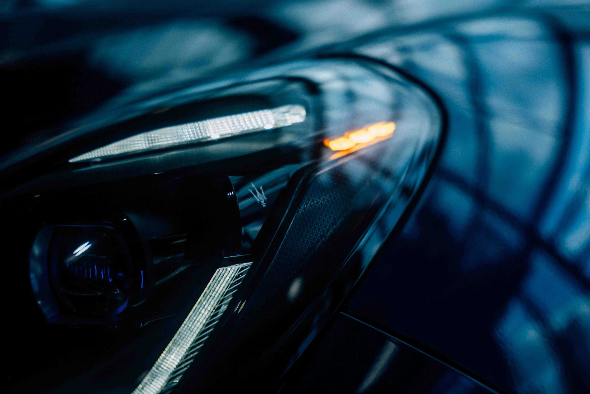 Close-up of a luxury car dashboard with illuminated controls and screens, featuring a sleek, modern design in a dark setting.