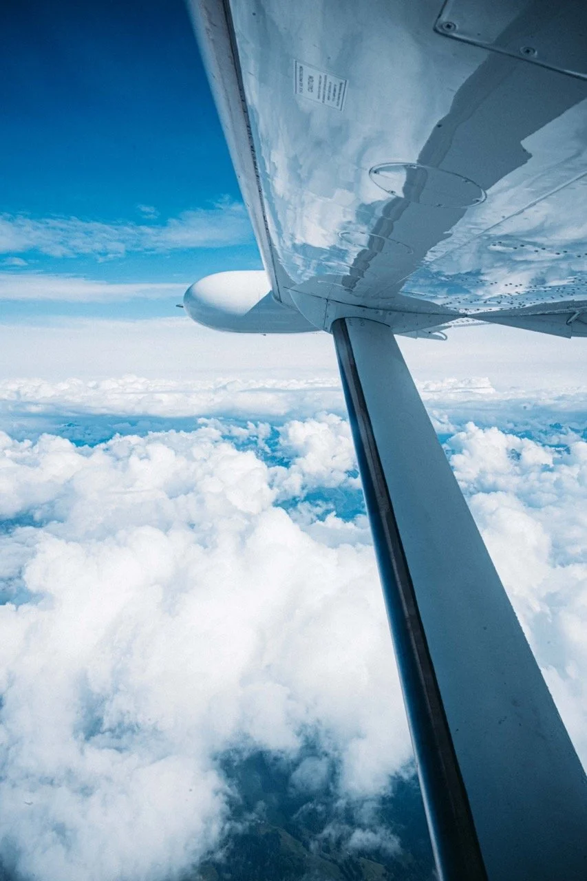 View from an airplane window showing the wing and a cloudy sky below.
