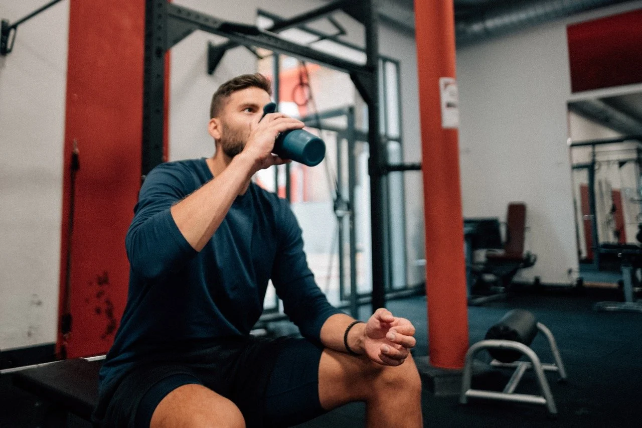 Man sitting on workout bench drinking water in a gym.