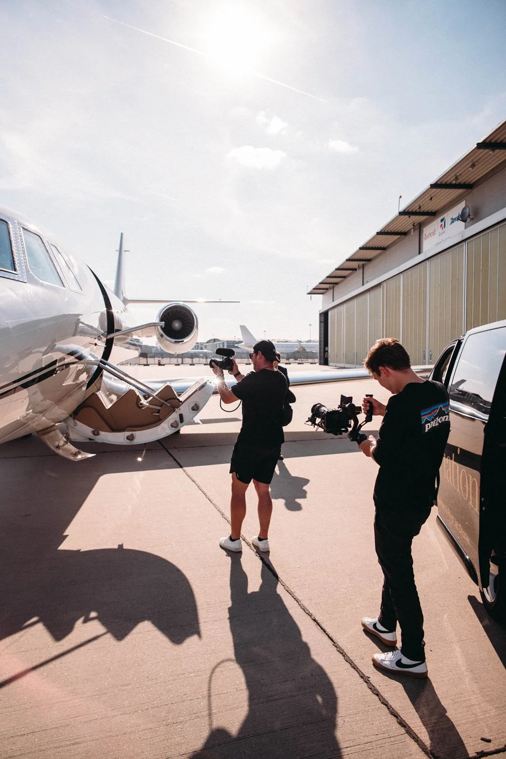 Two men filming a private jet on an airport tarmac during daytime.