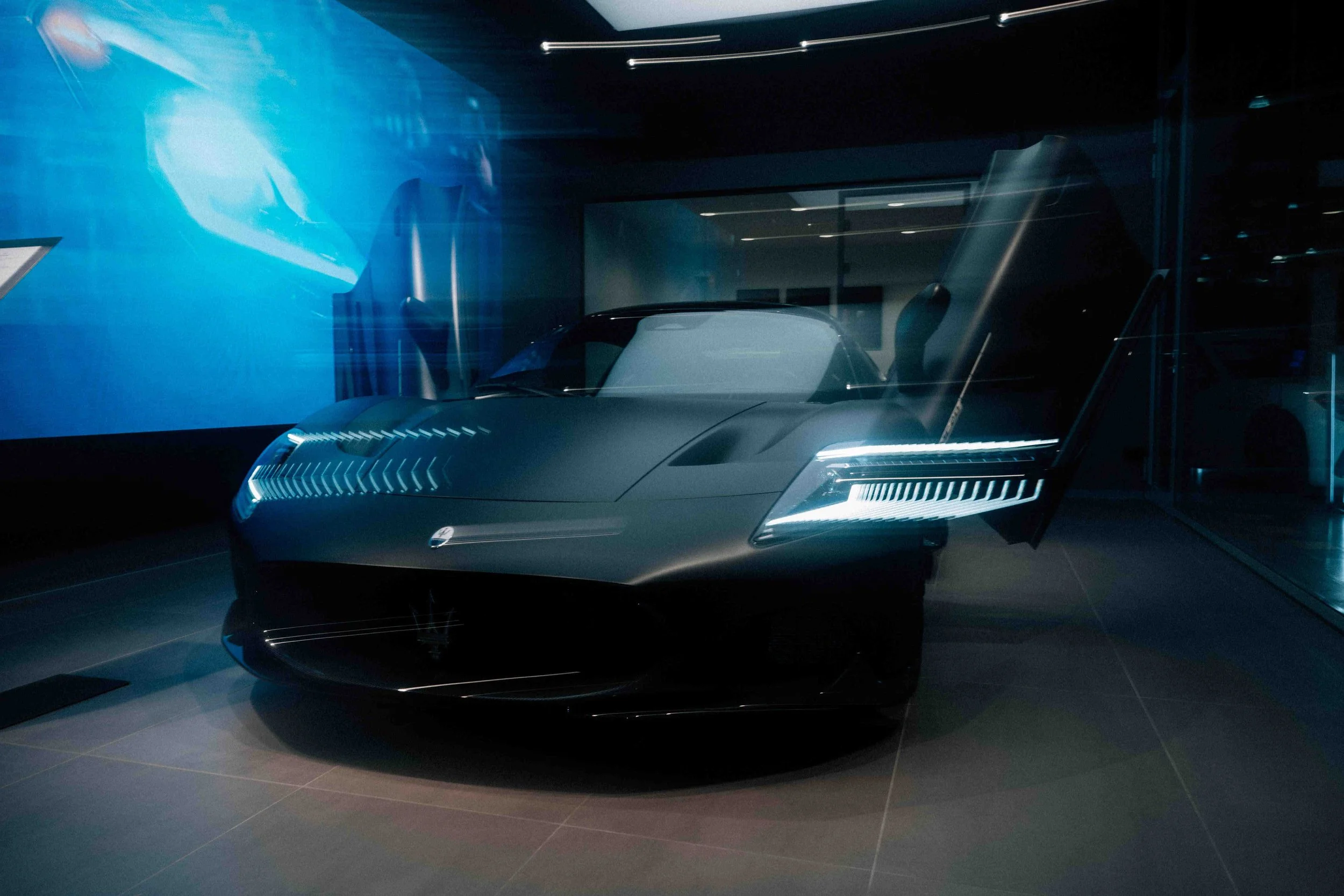 A sleek, futuristic black sports car with sharp angles and illuminated headlights, displayed in a modern showroom with reflective surfaces and blue ambient lighting.