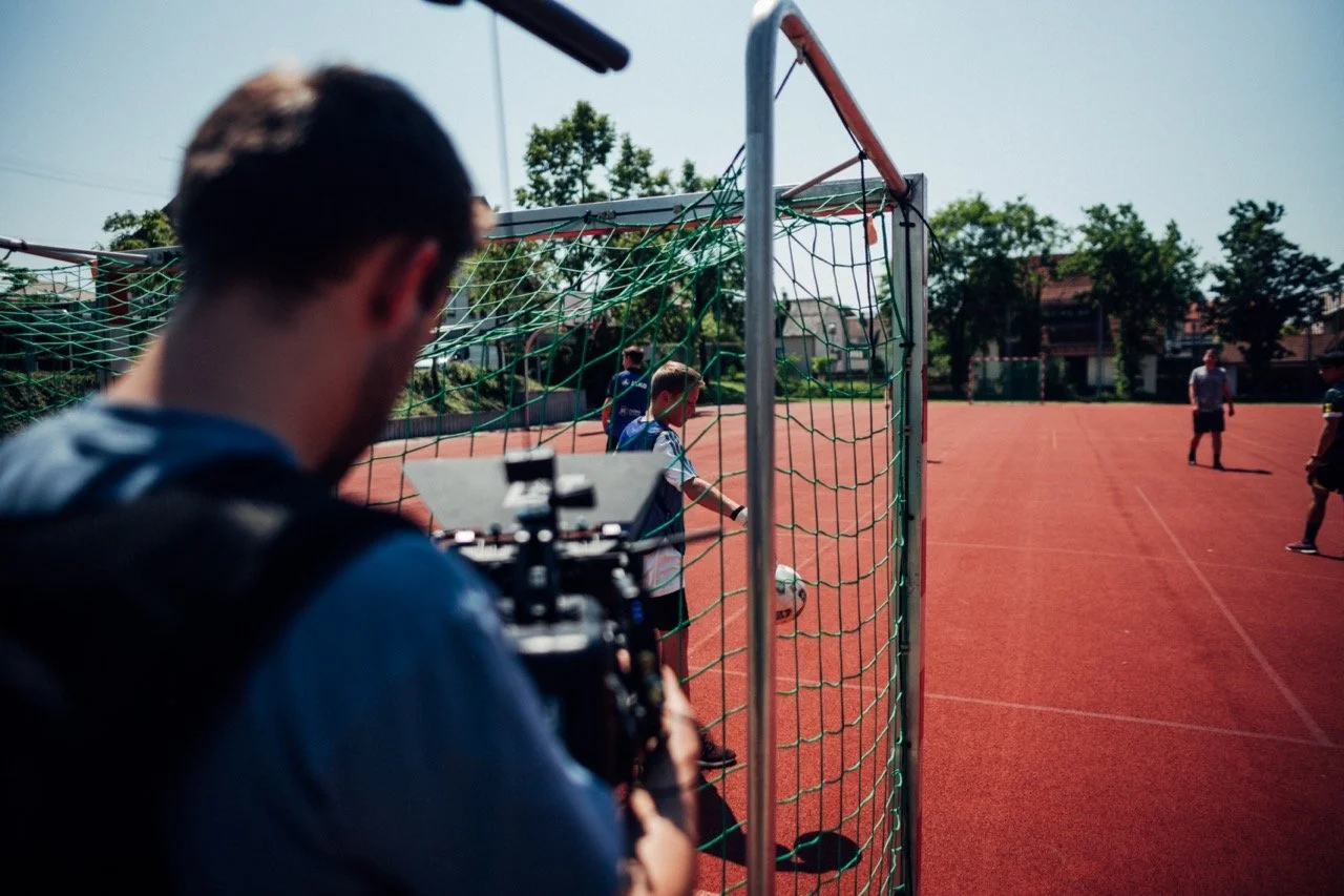 A person with a camera filming young soccer players on a field during daytime.