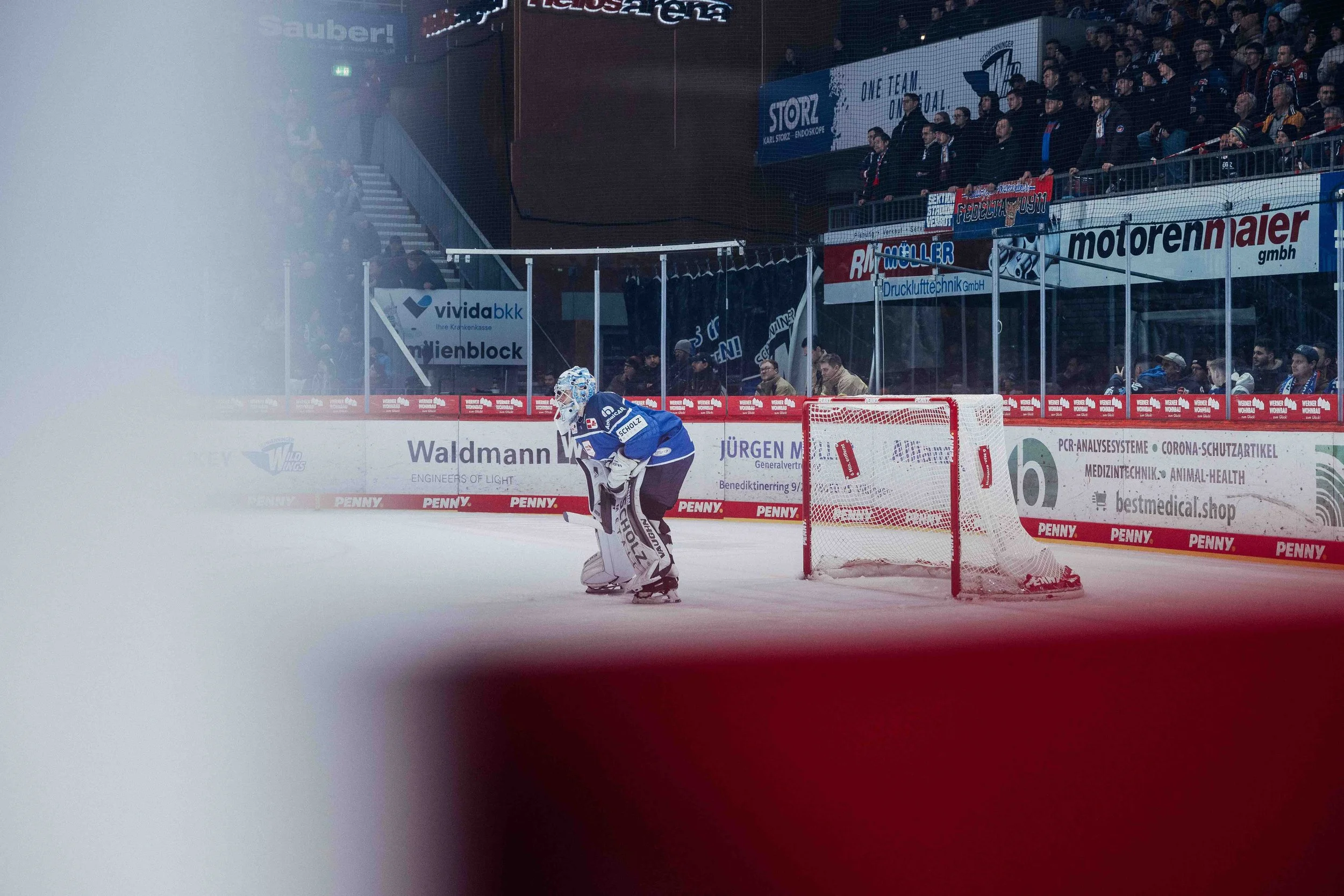 An ice hockey goalie in blue uniform standing in front of the net on the ice rink during a game.