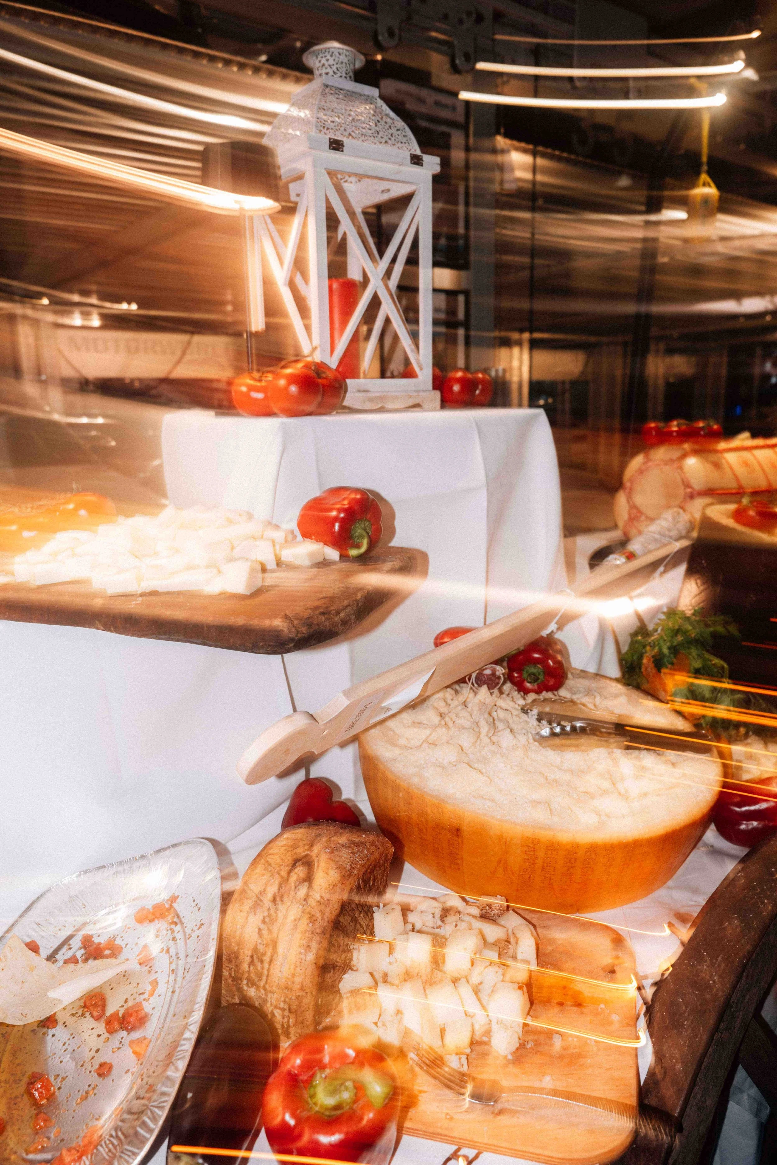 A display of cheese, vegetables, and bread on wooden boards and plates, with a white lantern and a white tablecloth, arranged in a rustic style.