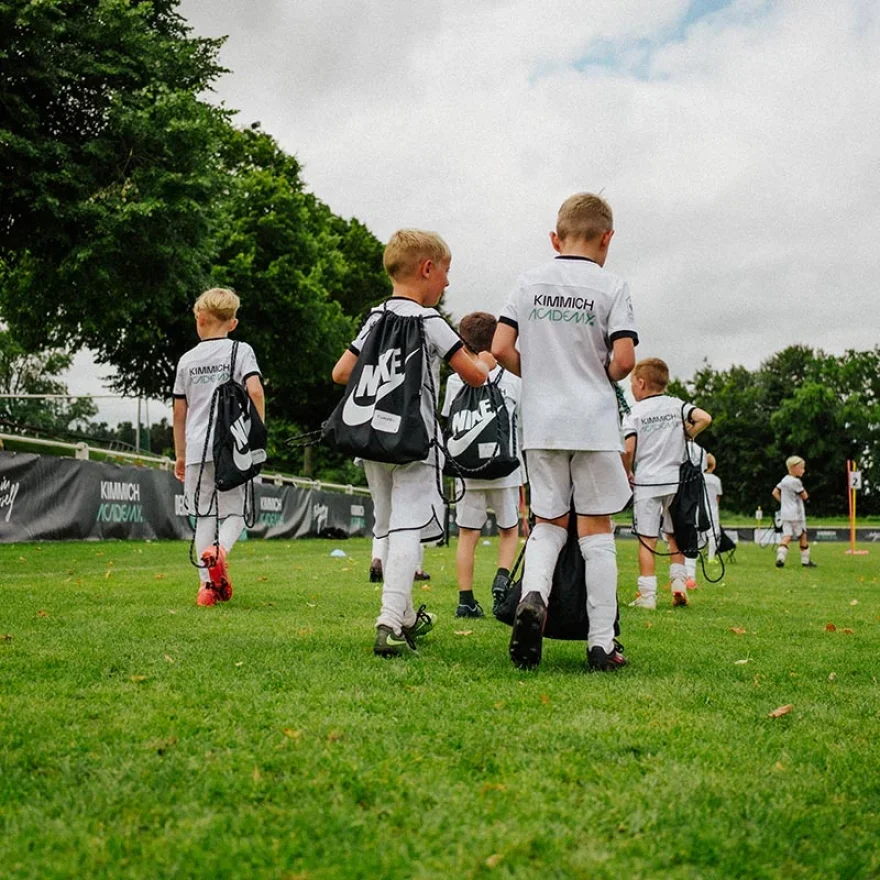 Young children in soccer uniforms walking on a field carrying Nike sports bags.