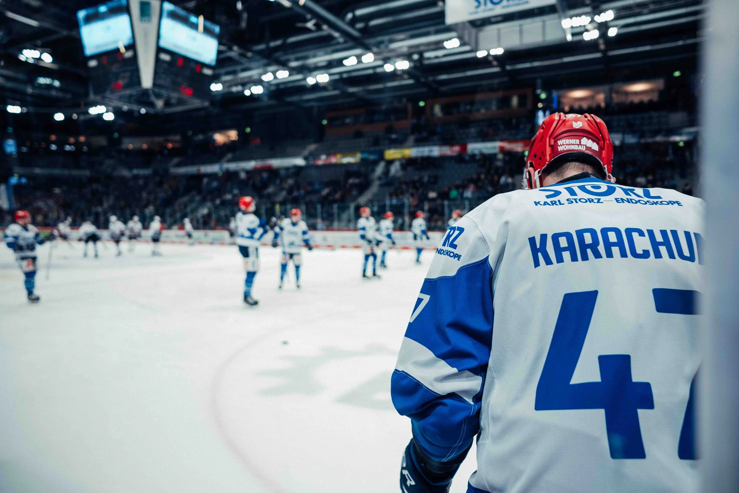 Hockey player in a jersey with  the number 47, standing on the ice with teammates warming up before a game in an indoor hockey arena.