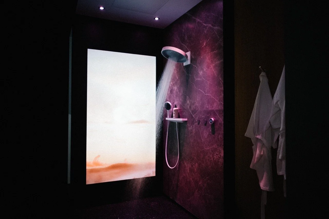 Modern shower with pink lighting, marble wall, and a digital screen in a dark bathroom.