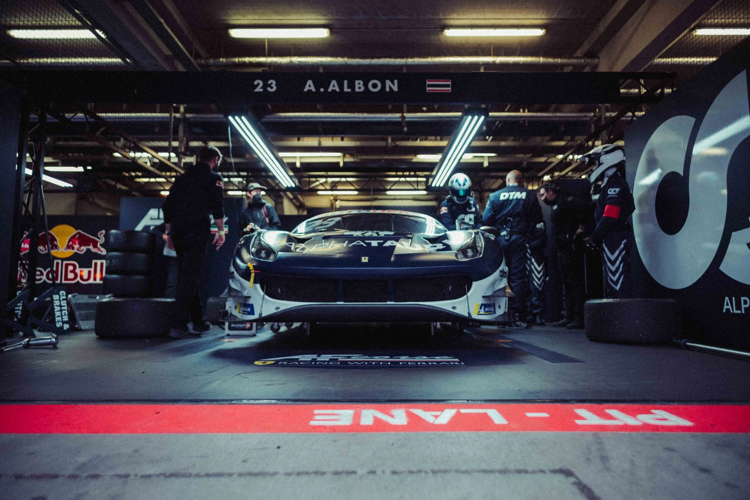 Race car inside the pit garage with mechanics and crew members working around it, with