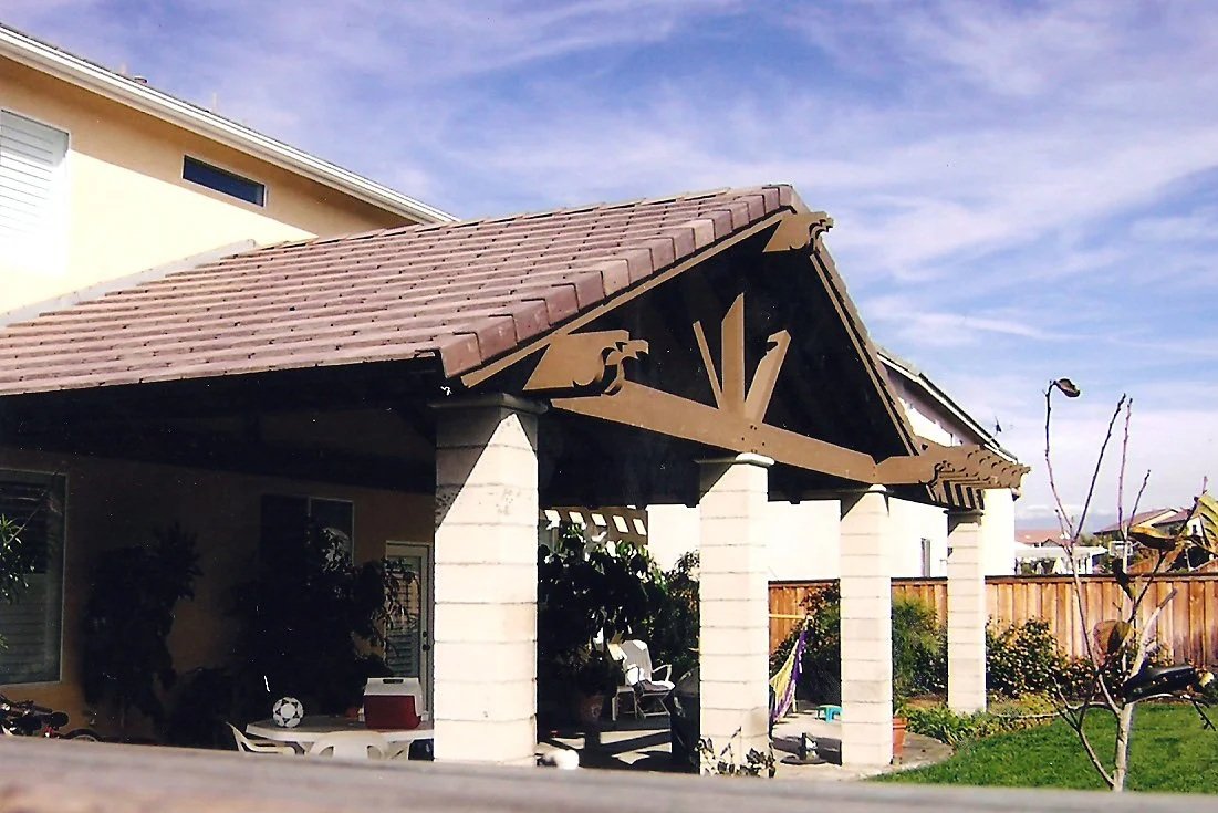 Backyard with a covered patio featuring decorative wooden beams, some chairs, clothes hanging, and a small table with a soccer ball.