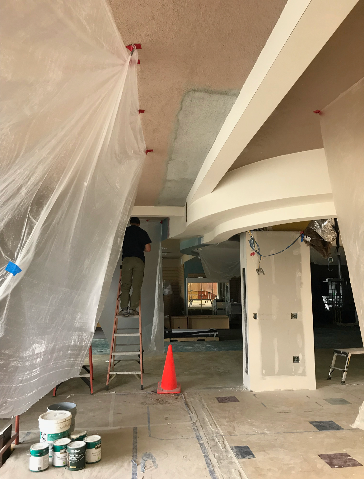 Interior renovation with a worker on ladder and construction materials, partially covered in plastic sheeting.