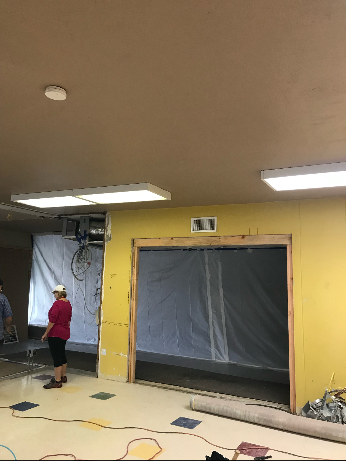 Interior of a building under construction with exposed wall framing, workers, and construction materials.
