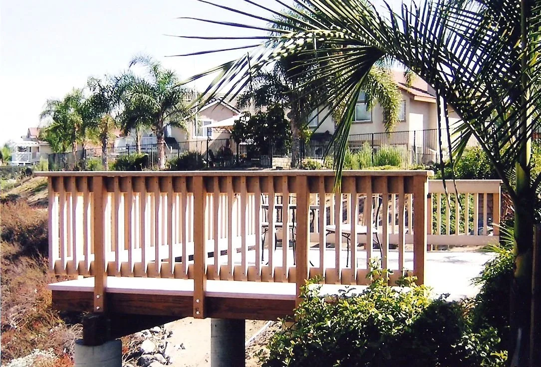 Wooden deck with outdoor patio furniture beneath palm trees in a residential neighborhood.