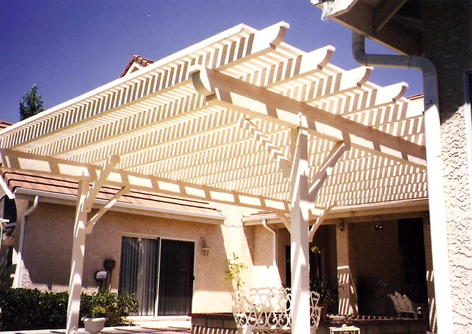 Backyard patio with a white pergola, sliding glass door, outdoor furniture, and some potted plants.