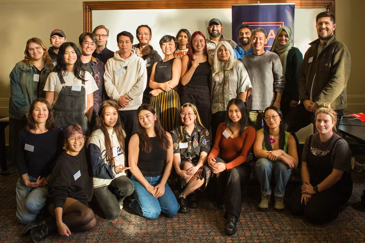 Group photo of about 24 people, largely of Asian descent, smiling, with a PASC banner behind them.