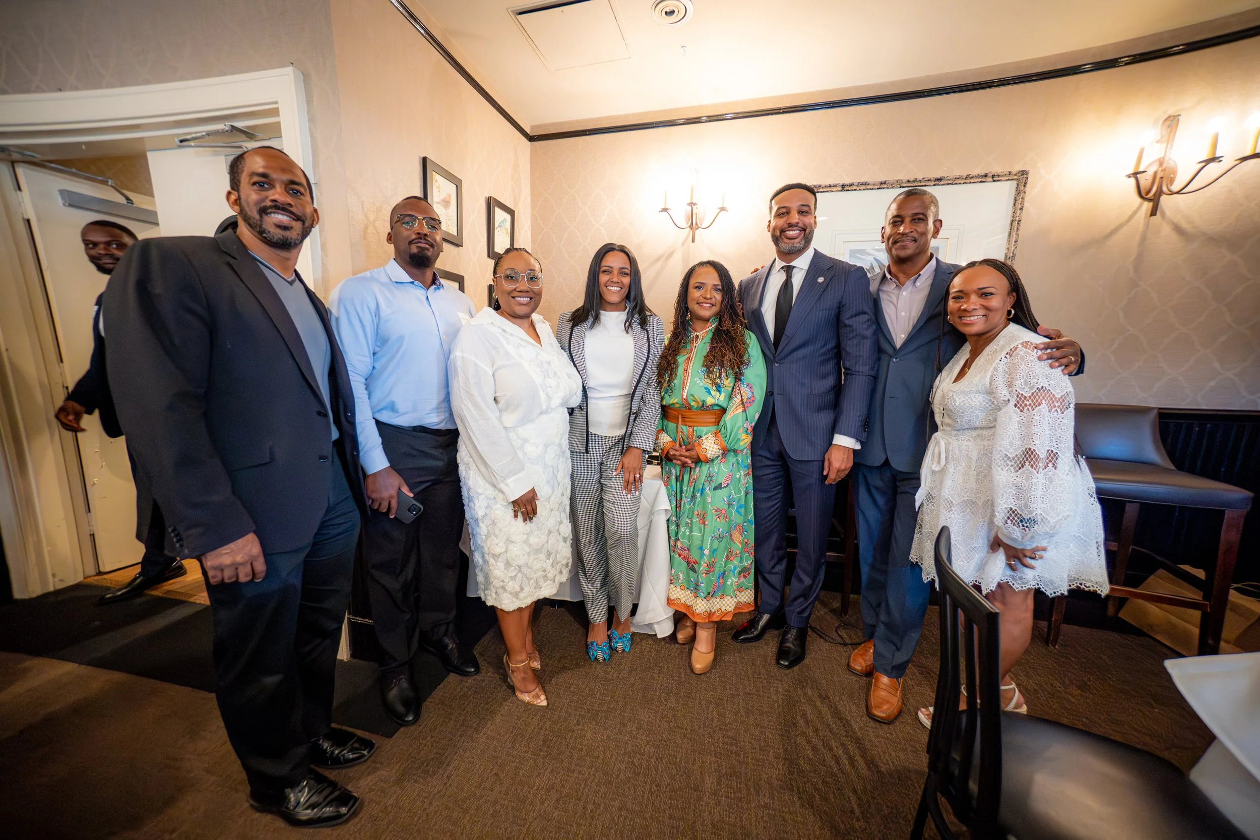 Group of nine diverse people in formal attire posing together in a restaurant or event venue.