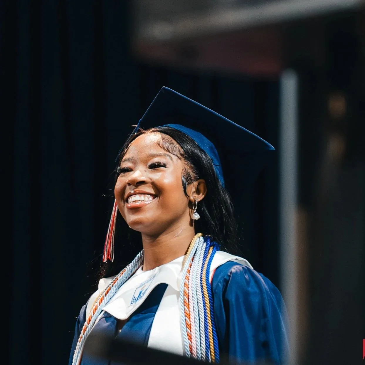 A young woman in a graduation cap and gown smiling at a graduation ceremony.