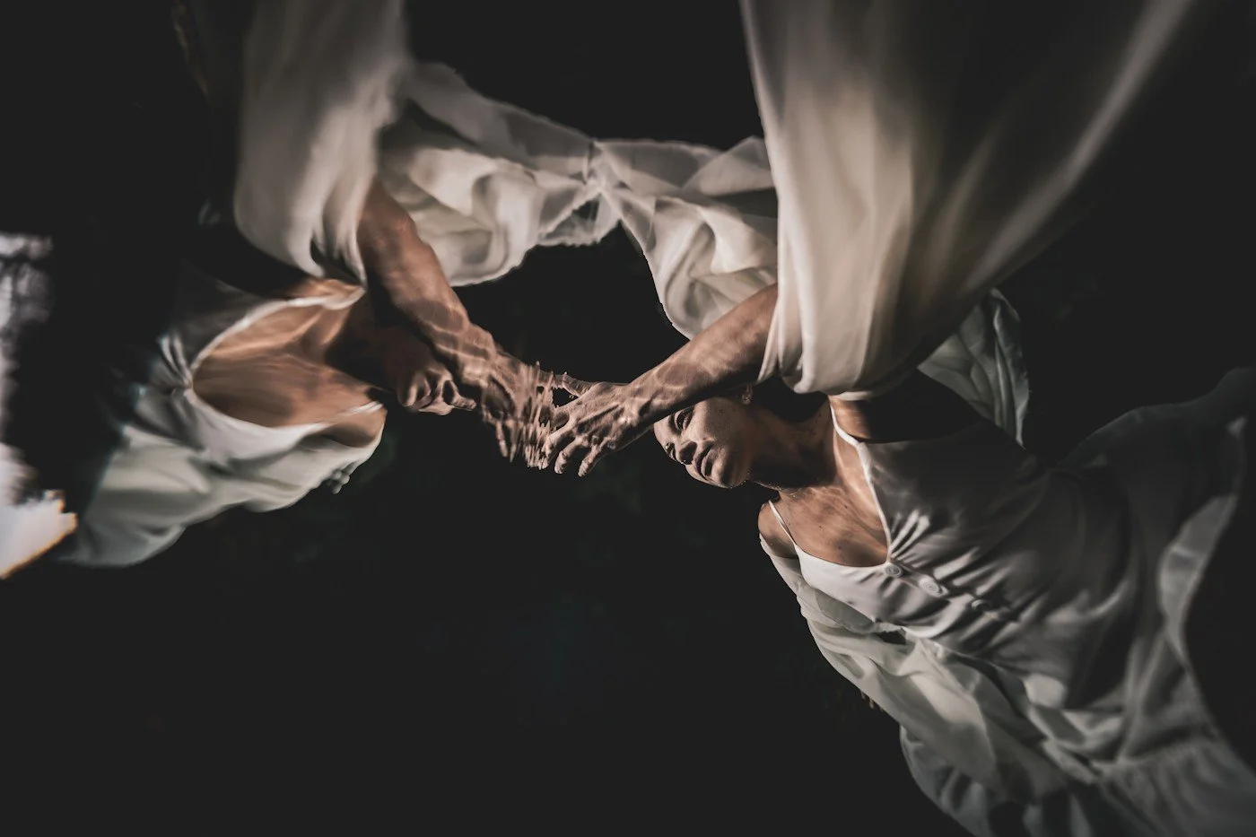A girl in a white dress underwater, in dark still waters that mirror her in this photo by Carpe Diem Holistic