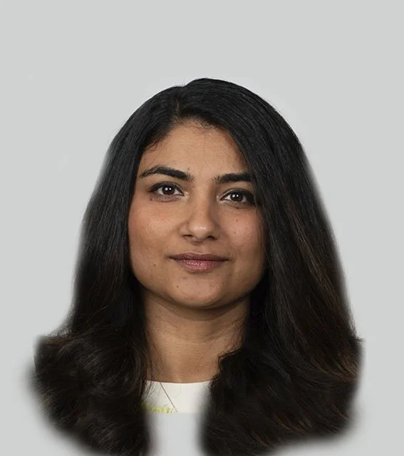 Portrait of a woman with long dark hair, wearing a white top, against a light gray background.